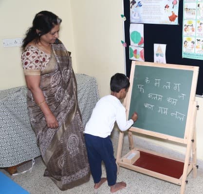 A teacher guiding a student writing on a chalkboard at Adra